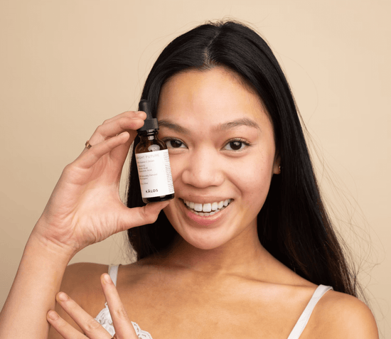 A smiling young woman holds up a small glass jar of a GreenMySkin product, showcasing her clear, radiant skin.