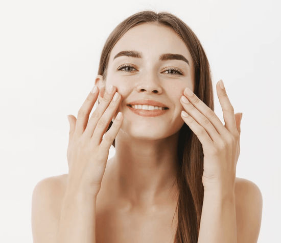 A smiling young woman gently applies a facial cream, her expression reflecting the nourishing and refreshing feel of the product from GreenMySkin.
