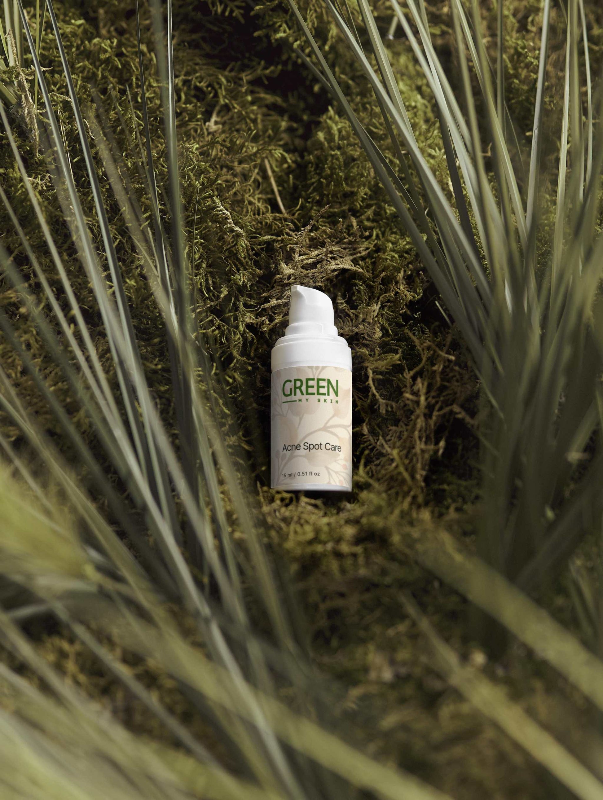 Acne Spot Care Serum bottle nestled in green foliage.