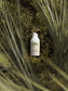Acne Spot Care Serum bottle nestled in green foliage.